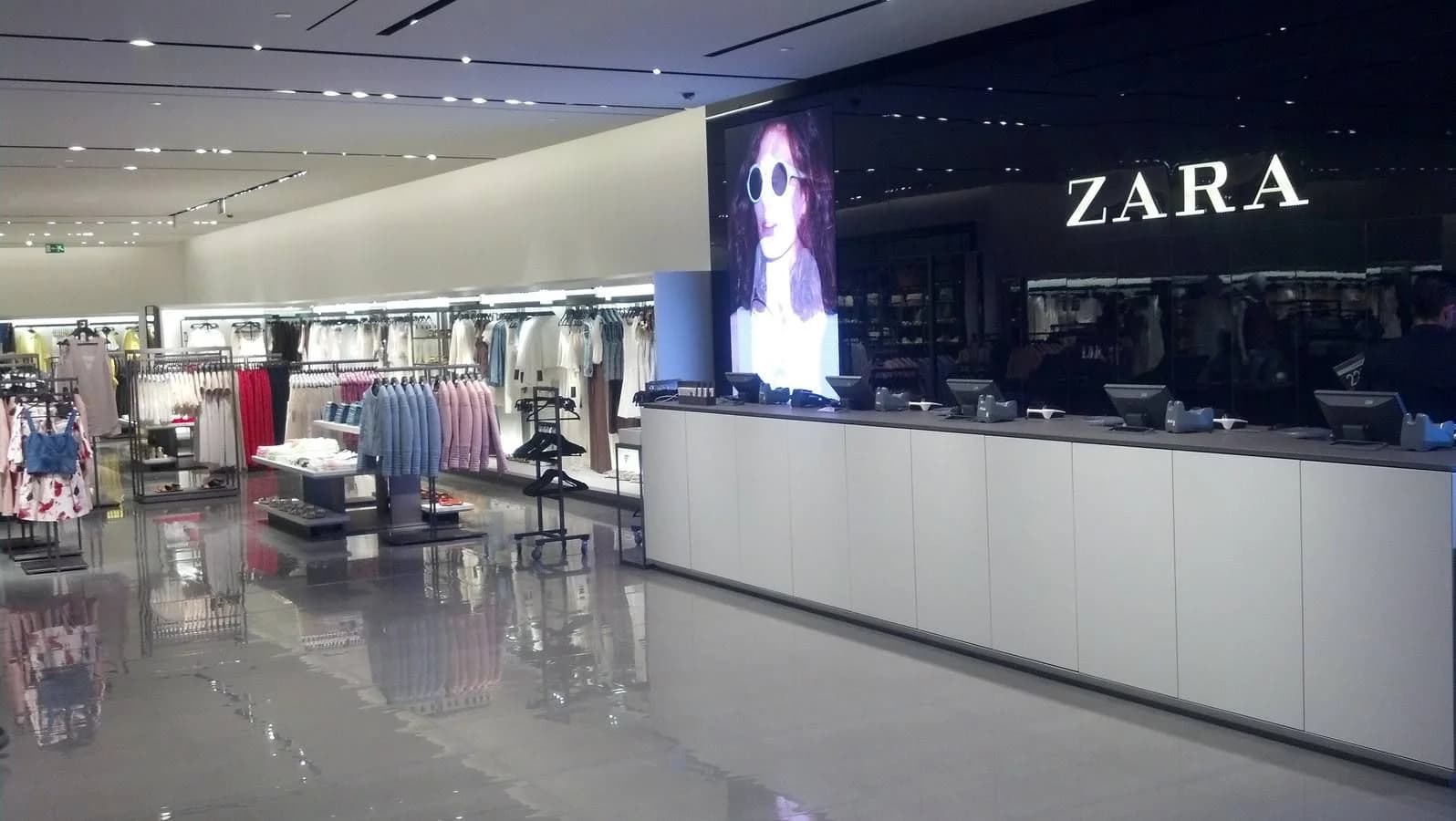 Amplio espacio de retail moderno con iluminación arquitectónica, en un plano cinematográfico de gran angular. La atmósfera es limpia y ordenada, con foco en la integración tecnológica de sensores de conteo de personas y hardware de seguridad discreto. La paleta está dominada por grises neutros y negros.
